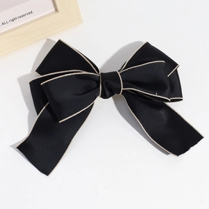 Detail of black satin bow hair clip with gold wavy edges on a white background