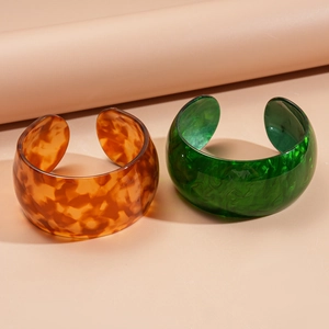Detail of wide resin cuff bracelets in amber tortoiseshell and green marble finish