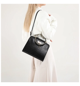 Detail of black crocodile texture handbag with golden round handle and deer pendant
