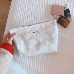 Close-up of white floral embossed fabric cosmetic bag with simple wish label on bed