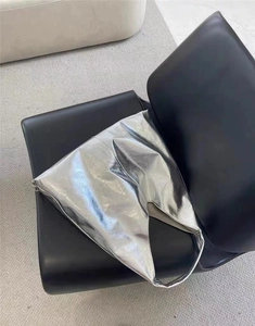 Sac Hobo argenté métallisé à grande capacité posé sur une chaise en cuir noir élégante