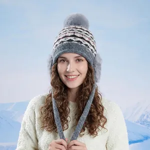 Bonnet tricoté gris avec pompon et protège-oreilles devant des montagnes enneigées