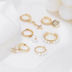 Six-piece gold earring set with pearl and star pendants on white silk background