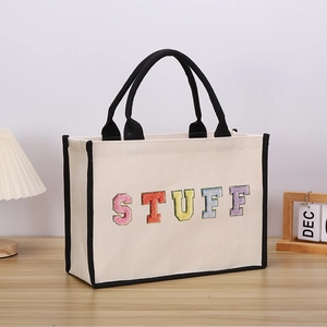 Close-up of colorful embroidered STUFF lettering on beige canvas tote bag with black handles