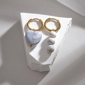 Boucles d'oreilles créoles dorées avec pendentif cœur marbré et perles sur support blanc