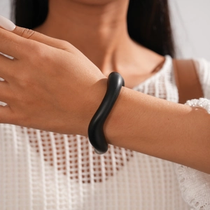 Detailed view of irregular wavy black acrylic cuff bracelet on model wearing white knit