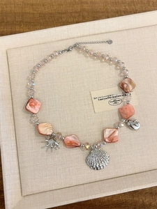 Detail of pink layered necklace featuring silver seashell charms and crystal beads