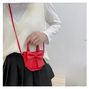 Detail view of a stylish red crossbody bag with a large bow worn by a model in white