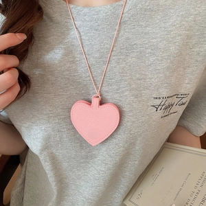 Close-up of pink leather heart pendant accessory on soft grey knitted sweater texture