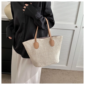 Detail of a large woven straw tote bag with brown leather handles and a textured beige finish