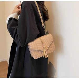 Detail of beige quilted crossbody bag with golden chain strap and tassel pendant