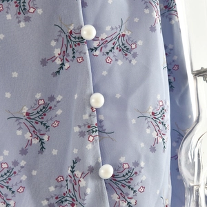 Gros plan détaillé de boutons en nacre blanche sur le tissu fleuri d'une robe bleue
