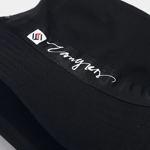 Détail d'un chapeau bob noir en toile avec ruban logo blanc et écusson géométrique
