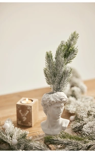 Detail of David statue vase with flocked snowy pine branch and soft candlelight