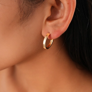 Close-up of a model wearing a polished gold geometric C-shaped earring with metallic luster