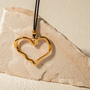 Detail of 18k gold irregular pleated heart pendant on a black cord necklace over stone