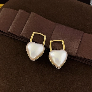 Élégantes boucles d'oreilles cœur en nacre dorée posées sur un fond de velours marron