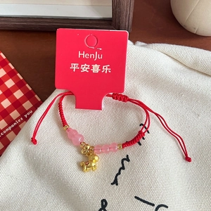 Detail of red braided bracelet with pink glass beads and golden zodiac charm on canvas