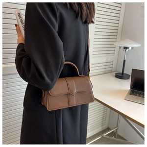 Chic brown leather shoulder bag shown in an office setting with a handheld strap