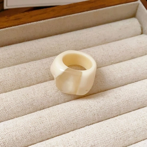 Detail of a wide resin ring in cream white with marble texture in a velvet jewelry box
