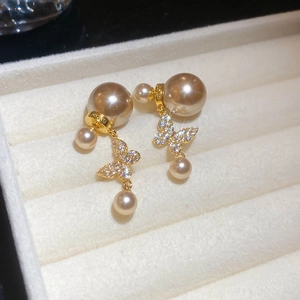 Macro shot of gold butterfly earrings with zircons and double pearls on velvet tray