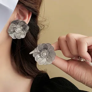 Large silver hollow flower earrings with radiant texture and central sparkling crystal