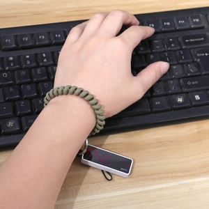 Dark green spiral spring keychain bracelet with floral pendant worn while typing on keyboard