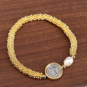 Macro detail of gold-tone Saint Benedict medal and pearl on religious bracelet