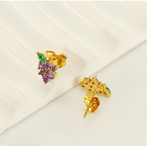 Macro detail of grape-shaped gold stud earrings with purple zircons and green leaf gem