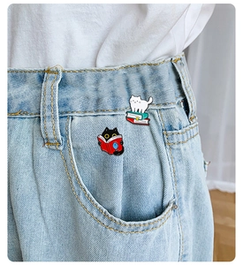 Detailed view of cat and book enamel pins pinned on denim jeans pocket background