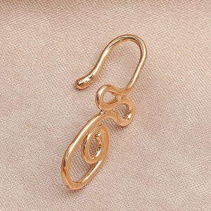 Détail d'un clip de nez doré en spirale en forme de U sur un fond de soie luxueuse
