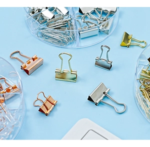 Flat lay of colorful binder clips and paperclips in a round clear organizer box