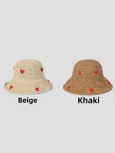 Detail of hand-woven straw hats in beige and khaki featuring red crochet hearts