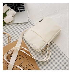 Close-up of small white nylon crossbody bag with adjustable strap and zipper closure