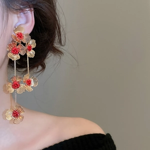 Macro detail of elegant golden layered flower earrings with red accents and long tassels