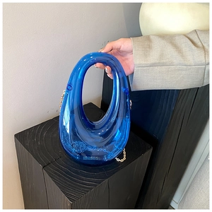 Close-up of blue transparent acrylic clutch bag with metal chain on a wooden base