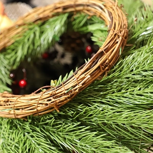 Close-up of Christmas wreath featuring red berries and realistic pine needles on a rattan base
