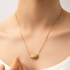 Detailed view of a gold hollow cylinder pendant with intricate vintage scroll patterns