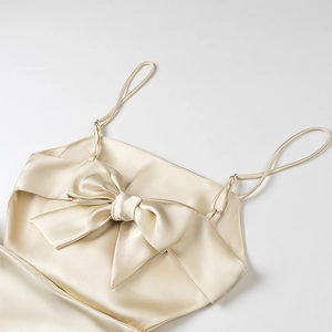 Detailed view of champagne satin dress featuring elegant oversized bow and thin straps