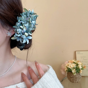 Detail shot of a blue-green fabric flower hair claw clip on a model's updo hairstyle