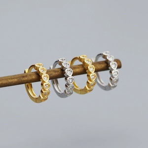 Detailed view of heart-shaped earrings in gold and silver hanging on a wooden rod
