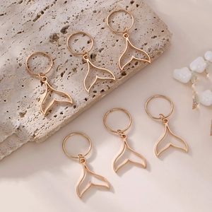 Detailed view of six golden whale tail hair pendants with rings on a stone background
