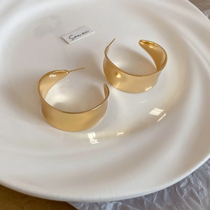 Detailansicht dicker goldener C-Form Creolen auf einer weißen Keramikschale