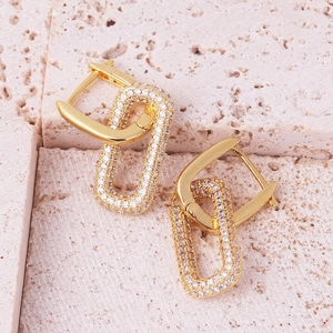 Detail of gold rectangular link earrings set with white cubic zirconia on a stone surface