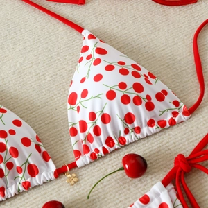 Detail of cherry print bikini top with red straps and small gold flower pendant on fabric