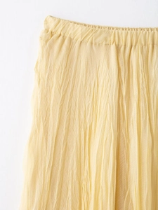 Detail of light yellow pleated skirt showing elastic waist and textured fabric