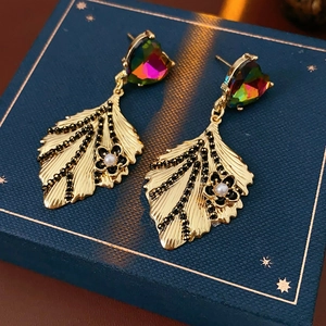 Macro detail of vintage gold leaf earrings with heart gems and pearls on a blue box