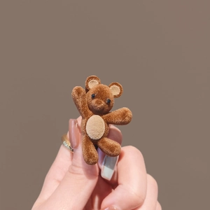 Cute brown flocked bear hair clip with waving pose shown in hand for side bangs
