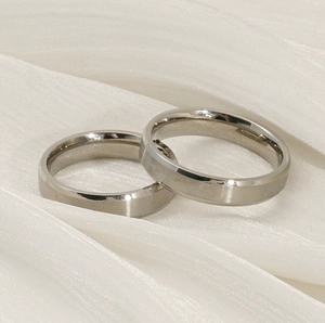 Macro shot of two minimalist silver titanium steel rings on white silk fabric background