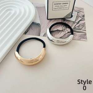Close-up of golden and silver metallic hair ties on a minimalist tray background